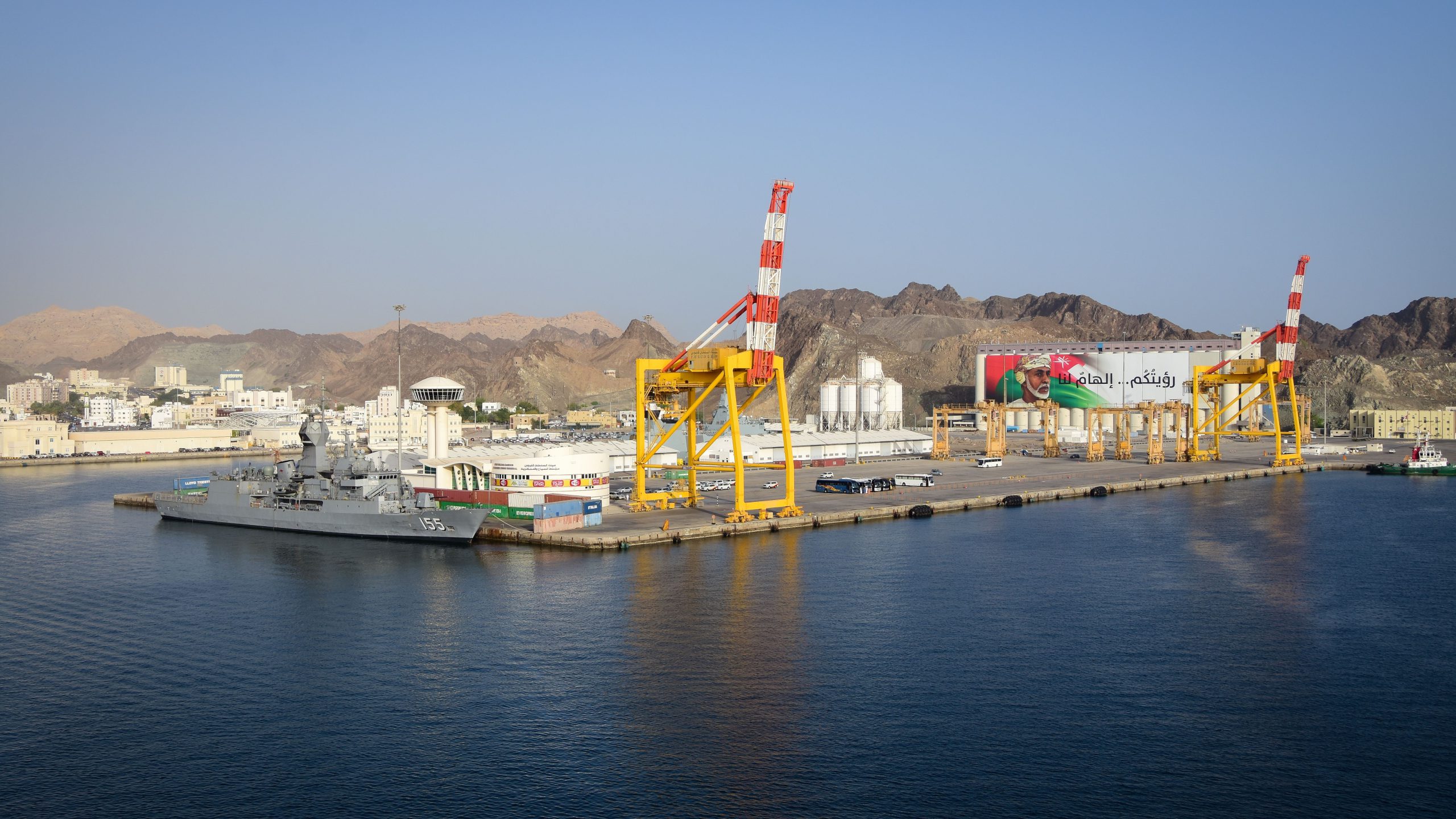 Aerial view of Muscat port with ship, cranes, and mountains in Oman.
